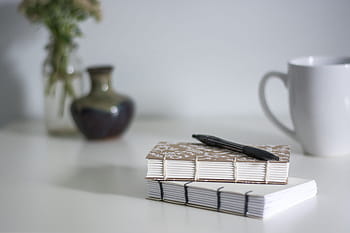notatbok, personlig journal, skrive notatbok, skrivebord setup, kaffekopp, penn og notisbok, minimalistisk arbeidsplass, blomstervase, hvitt bord, kreativt arbeidsområde, daglig planlegger